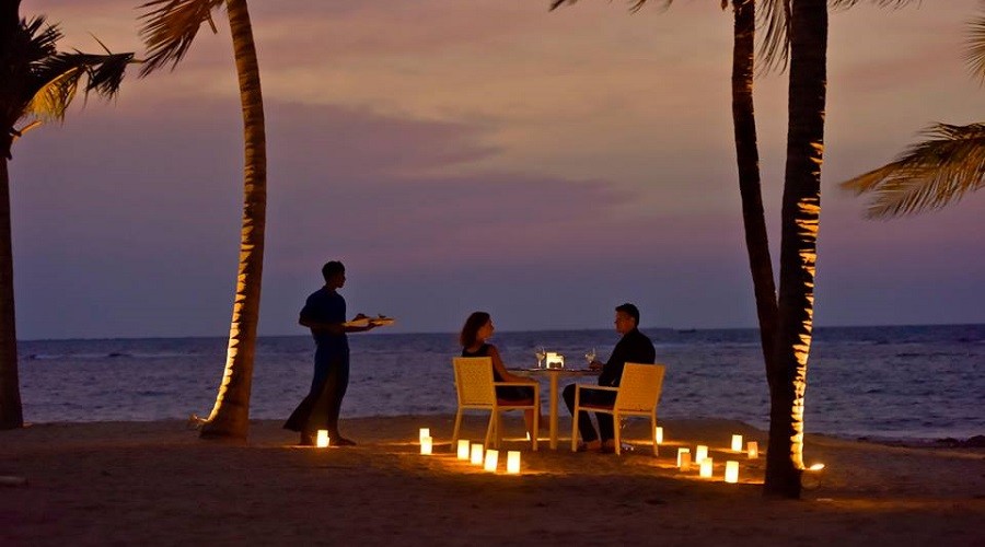 Beach dinner setup with a couple and waiter serving. Candled walkway to the table at the sunset hour at Sun Aqua Pasikudah