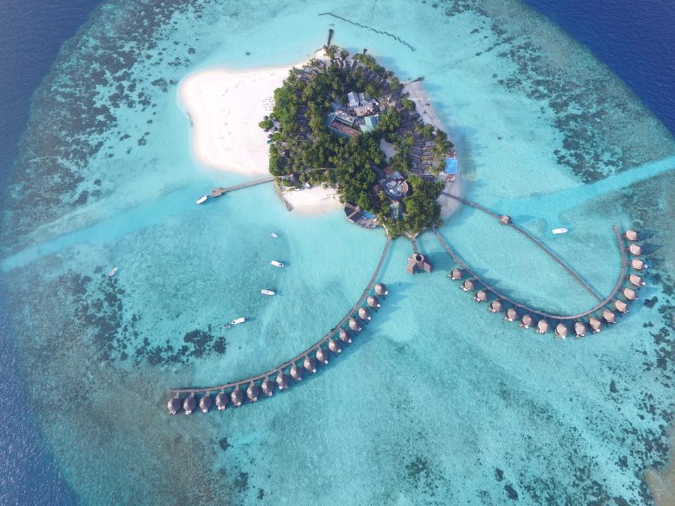 birds eye view image of a madivian resort with turquoise waters and white sandy beaches