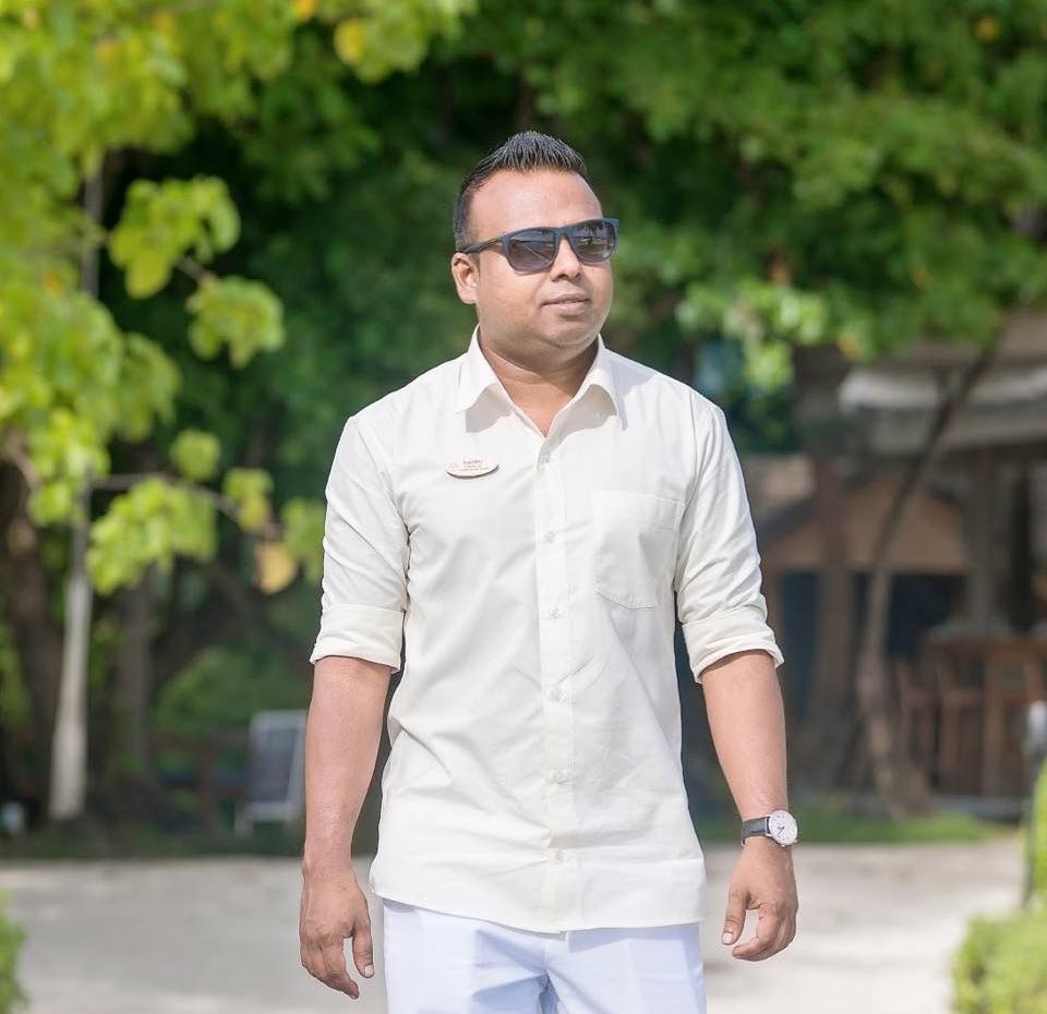 Nasrulla Adam , the new director of sales walking towards the camera. with black shades on a sunny day and green lush back ground.