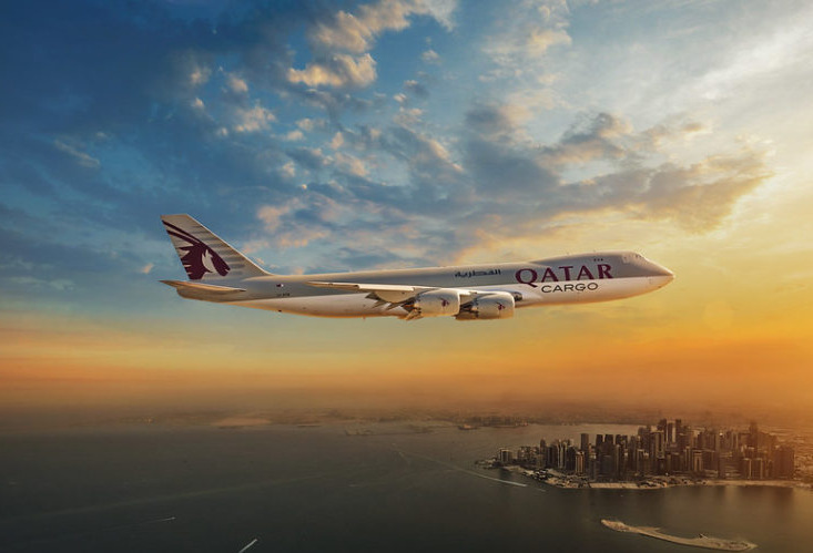 Qatar Airways cargo aircraft Boeing 747, flying over a city.