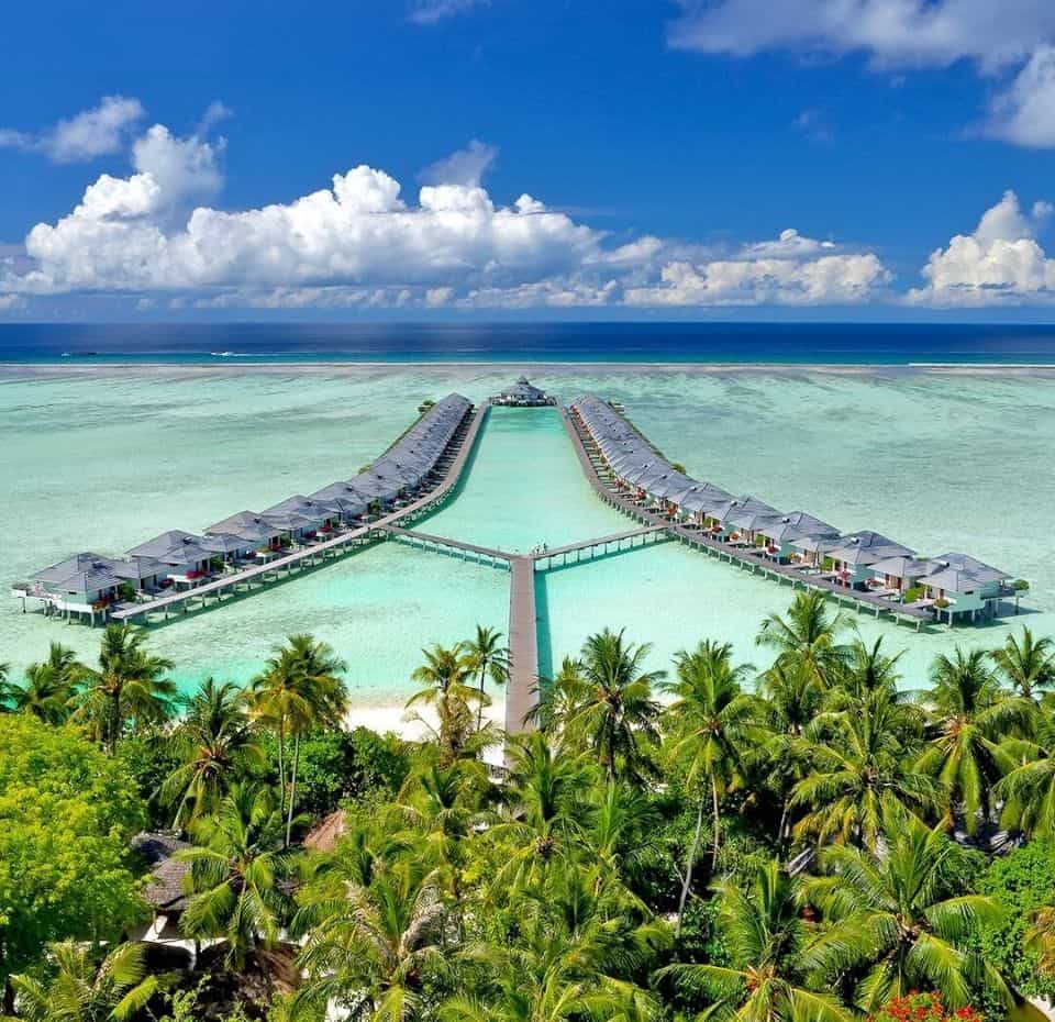 drone image of Villa hotels ans resorts at sunisland, showing over water villas with shades of blue and lush green palm trees