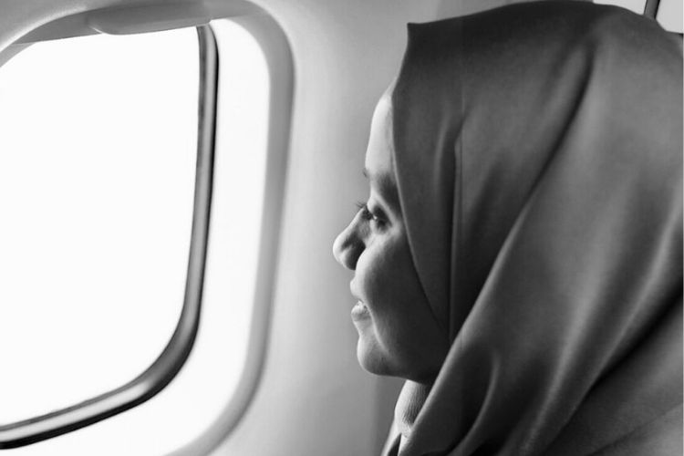 Alaa from FLYME , a woman in veil looking out of a airplane window